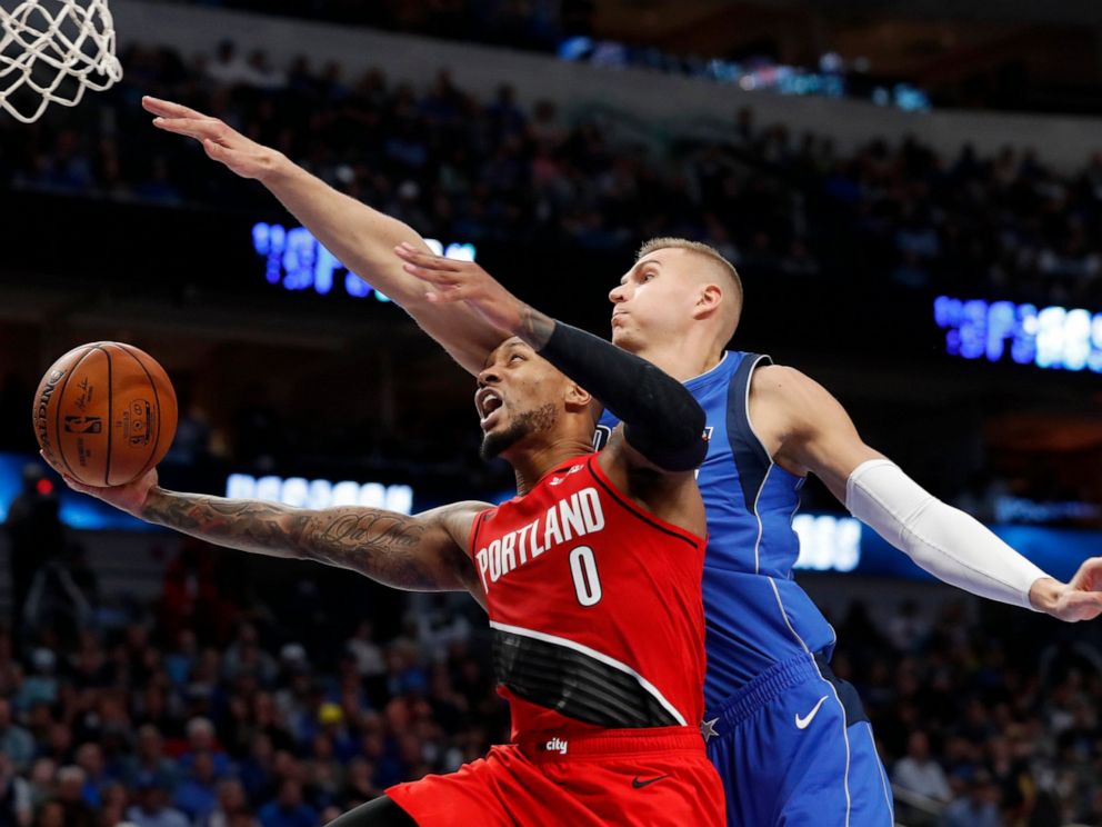 Kristaps Porzingis attempts to block a layup from Damian Lillard in a matchup between the Mavericks and Trail Blazers